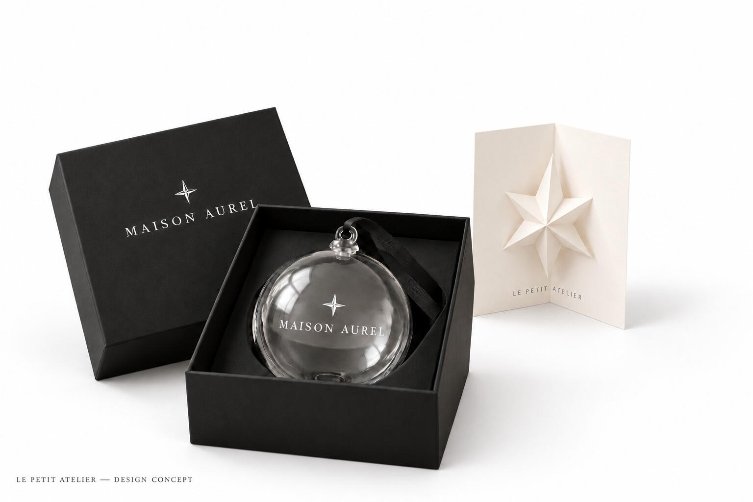 MAISON AUREL seasonal concept: glass Christmas ornament with white printing, black gift box and sculptural star greeting card on a white backdrop.